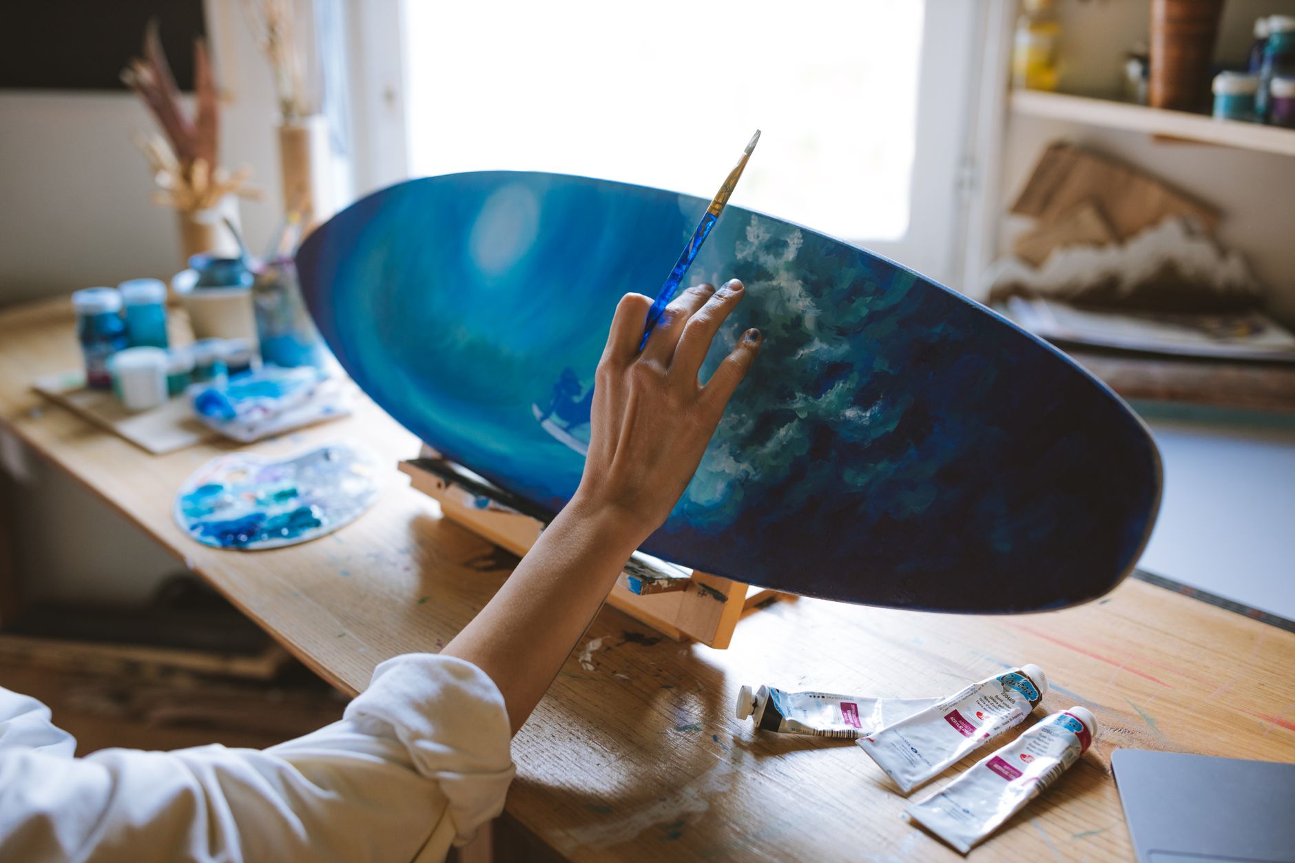 Close-up of an artist painting a surf-themed surfboard in a creative studio setting in Carlsbad, CA